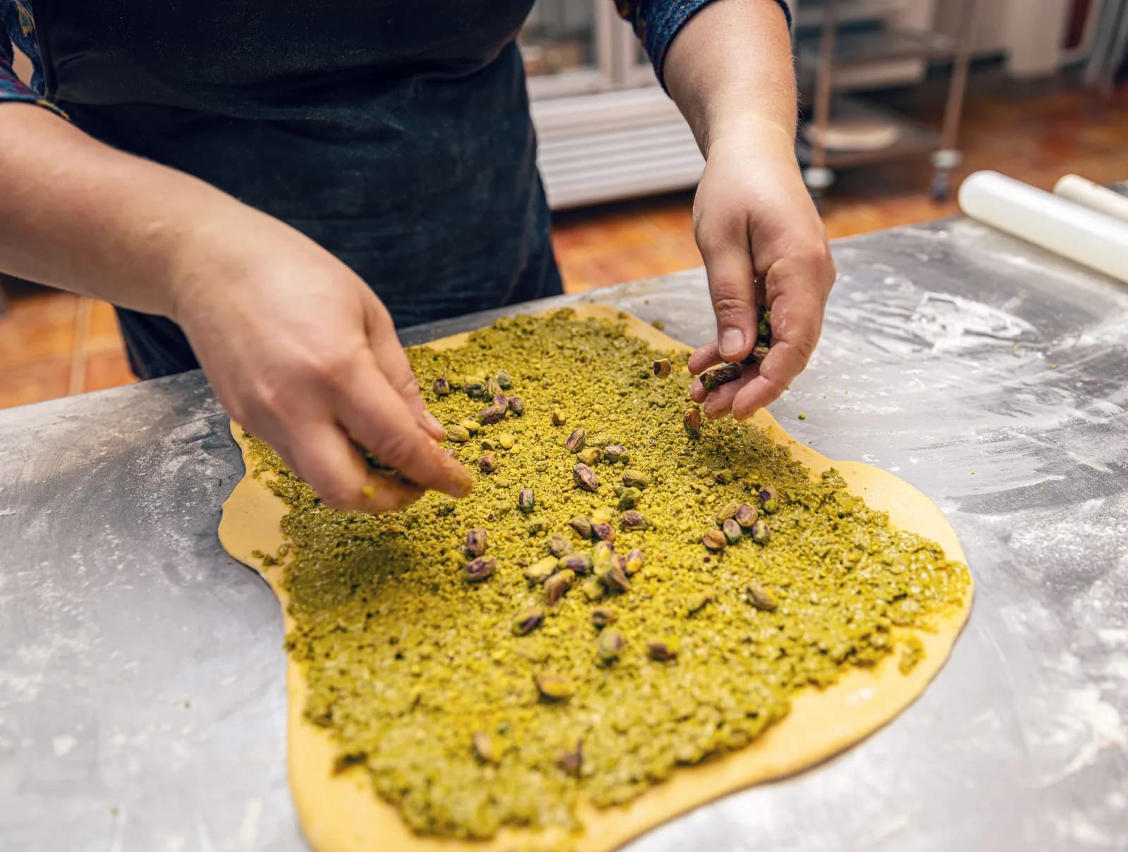 Konditor rollt hauchdünnen Baklava-Teig von Hand aus und verteilt gemahlene Pistazien darauf
